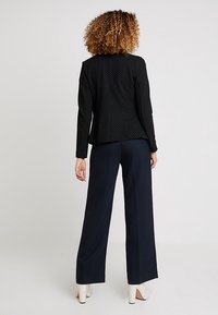 Černý blazer s puntíky a pohodlným střihem, spárovaný s námořnickými kalhotami s širokými nohavicemi a krémovými botami na blokovém podpatku. Hladká tkanina, moderní silueta.