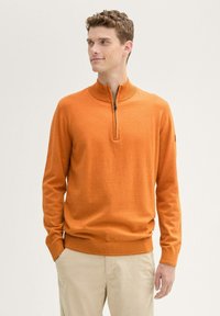 Orange Zip-Up-Pullover mit hohem Kragen, langen Ärmeln und geripptem Saum. Der Stoff wirkt glatt mit einer subtilen Textur; keine sichtbaren Muster.