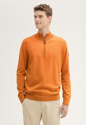 Orange Zip-Up-Pullover mit hohem Kragen, langen Ärmeln und geripptem Saum. Der Stoff wirkt glatt mit einer subtilen Textur; keine sichtbaren Muster.