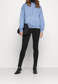 Světle modrá mikina s kapucí a přední kapsou, spárovaná s černými legínami a černými kotníkovými botami, vytvářející ležérní vrstvený vzhled.