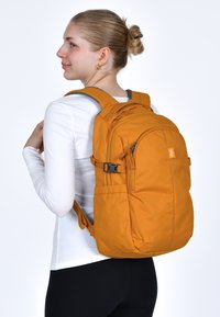 Zaino di tessuto arancione con spallacci imbottiti, tasche frontali con zip e regolatori laterali. Texture liscia con un design robusto.