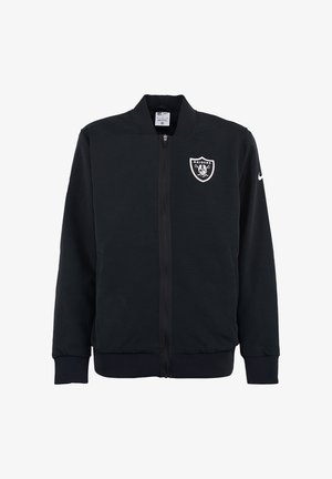 Czarna kurtka zapinana na zamek, wykonana z gładkiego materiału, z logo Raiders na piersi i stójką. Rękawy i dół są ściągacze.