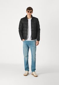 Jachetă neagră căptușită cu fermoar în față, purtată peste un tricou alb, asortată cu blugi albaștri deschiși și adidași bej. Modelul poartă ochelari de soare.