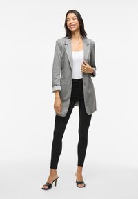 Blazer grigio con maniche arrotolate, chiusura a singolo bottone e tasche frontali, abbinato a jeans skinny neri e tacchi aperti.