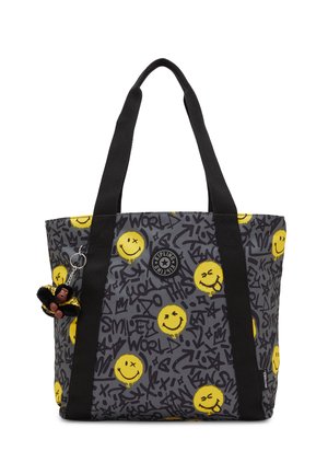 Szara torba typu tote z czarnym tekstem w stylu graffiti, żółtymi buźkami, czarnymi uchwytami i małą brelokiem w kształcie małpki przymocowanym do jednego uchwytu.