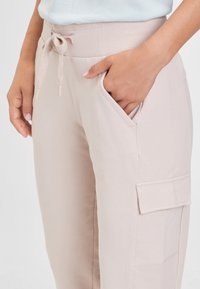 Lichtroze, zachte stoffen broek met een aansnoerbare taille, zijzakken en een cargozak op de dij. Glad textuur en een relaxte pasvorm.
