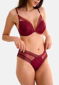 Soutien-gorge bourgogne avec bordure en dentelle et bretelles réglables, associé à des culottes assorties avec des accents en dentelle et des panneaux transparents. Texture lisse.