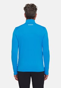 Długi rękaw niebieskiej koszulki sportowej wykonanej z elastycznej tkaniny z wysokim kołnierzem i logo z tyłu, z dopasowanymi rękawami i płaskimi szwami.