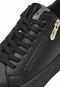 Sneaker nera con tomaia in pelle liscia, superficie texturizzata, lacci piatti, zip laterale e dettagli in vernice lucida.