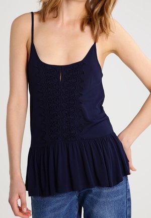 Marineblaue Camisole mit dünnen Trägern, ausgestattet mit einem Spitzenbesatz in der Mitte und einem ausgestellten Saum. Glatte Textur, lässige Passform und leichter Stoff.