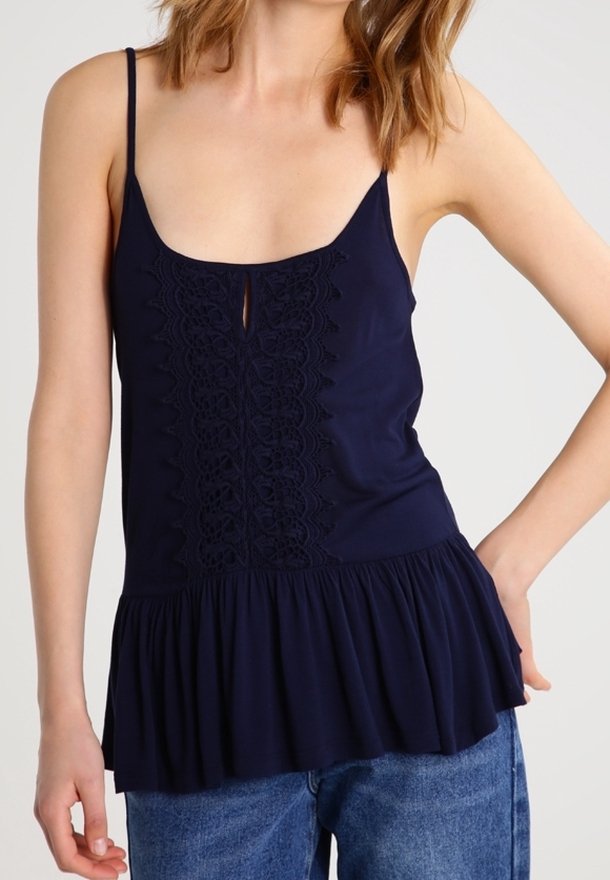 Camisole bleu marine à fines bretelles, avec un panneau en dentelle au centre et un ourlet évasé. Texture lisse, coupe décontractée et tissu léger.