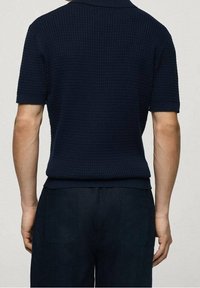 Tmavě modré pletené polo tričko s krátkými rukávy, límečkem na plochu a texturovaným vzorem. Pohled zezadu ukazuje přiléhavý střih a jednoduchý lem.