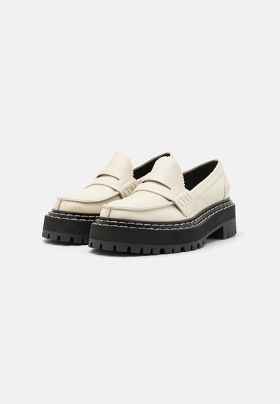 Valged nahast loafers musta paksu kummitaldadega, dekoratiivse õmblusega ja lainelise äärisega keelega.
