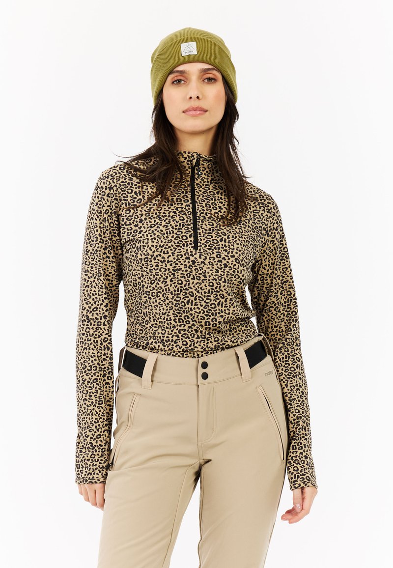 Camiseta de manga larga con estampado de leopardo y cremallera negra, combinada con pantalones beige con acentos negros y bolsillos delanteros. Gorro verde oliva en la cabeza.