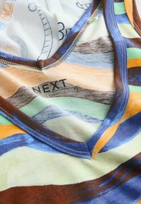 Primer plano de tela a rayas coloridas con costuras reforzadas y etiqueta impresa "NEXT" en material suave.