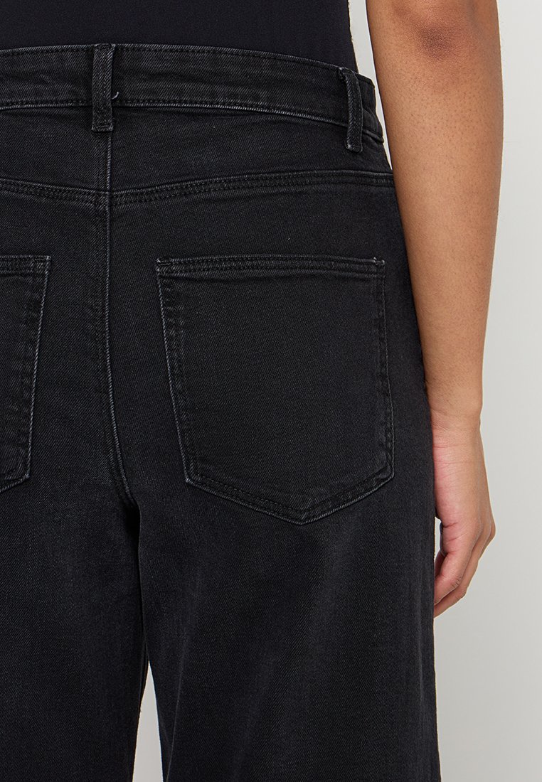 Zwarte denim jeans met een hoge taille, zichtbare achterzakken en een glad, gestructureerd oppervlak. De stiksels zijn subtiel en komen overeen met de kleur van de stof.