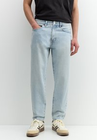 Hellblaue Jeans aus Denim mit einer lockeren Passform, fünf Taschen, Knopfverschluss und dezentem Verblassen, kombiniert mit cremefarbenen Sneakers.
