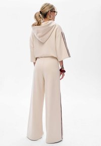 Beige, oversized hoodie met korte mouwen, gecombineerd met bijpassende wijdvallende broek met een bordeauxrode streep langs de zijkanten. Gladde textuur.
