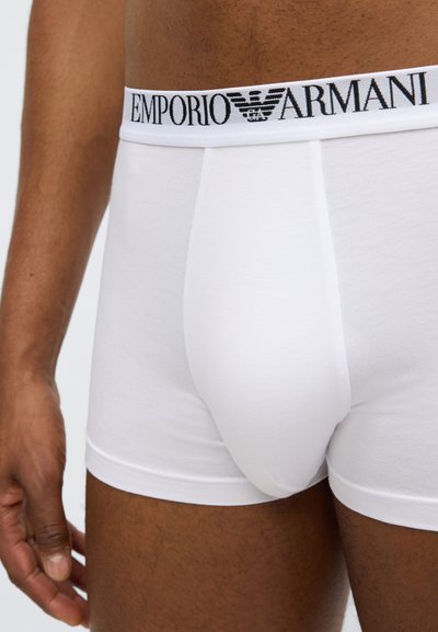 Boxers blancs en coton avec une ceinture noire arborant le logo Emporio Armani, offrant une coupe ajustée et une texture lisse.