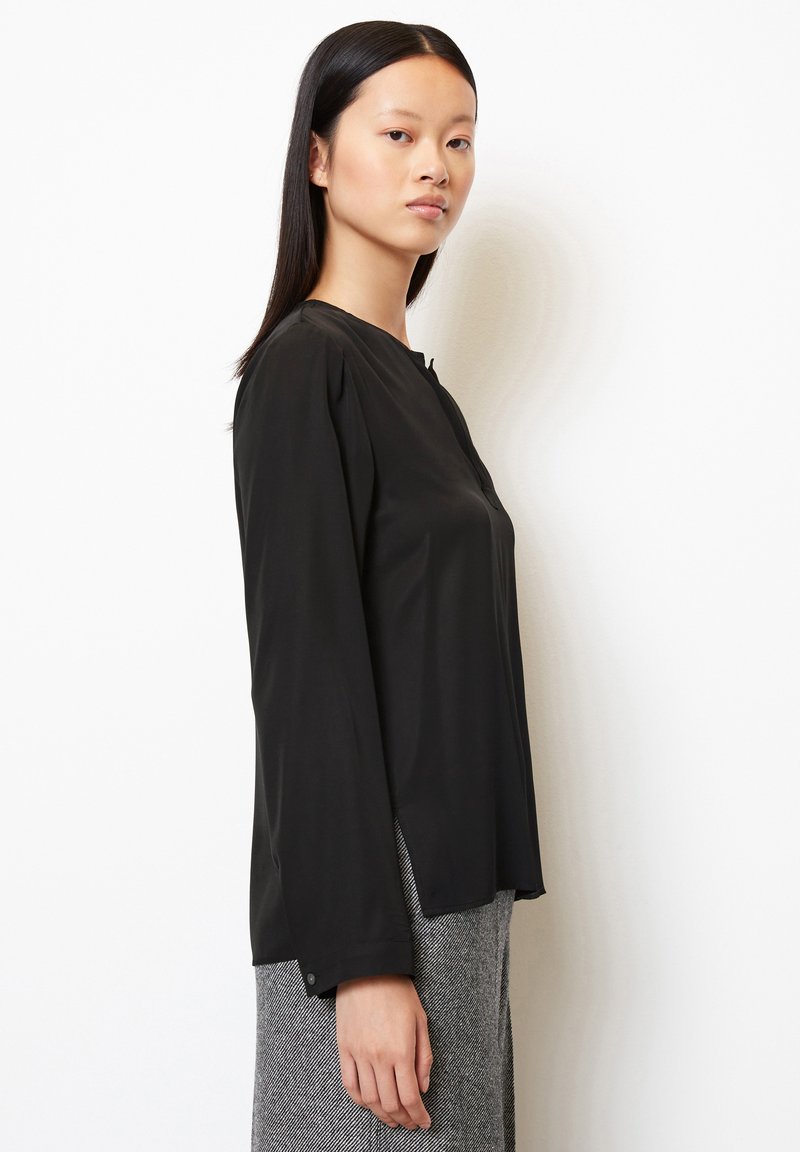 Czarna bluzka z długim rękawem z lekkiego materiału, z okrągłym dekoltem, delikatnymi plisami na ramionach i zapięciem na guziki przy mankietach.