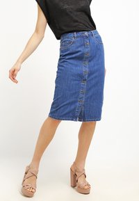 Denim-mekko hame, jossa on vaaleansininen pesu, etupuolella napitus, kaksi taskua ja keskipitkä malli.