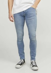 Jeans skinny din denim de culoare albastru deschis, cu o textură netedă și design cu cinci buzunare, asortați cu adidași negri înalți și un tricou alb.