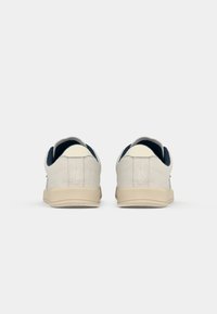Hvite semskede sneakers med marineblå detaljer, flate såler og sydde detaljer på baksiden. Glatt tekstur med minimale designfunksjoner.