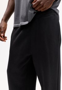 Zwarte broek met elastische tailleband en zijzakken, gecombineerd met een grijs T-shirt met korte mouwen en een ronde zoom met contrasterende stiksels.