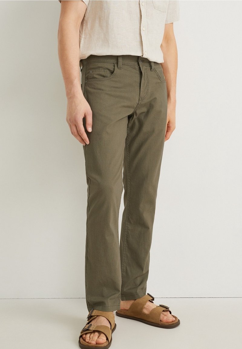 Pantalones de algodón verde oliva con corte recto, que cuentan con cinco bolsillos y una cintura de altura media, combinados con sandalias marrones.