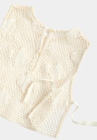 Top de crochet sin mangas de color crema con patrones hexagonales y de hojas, cierre de botones en la espalda y lazos laterales ajustables.