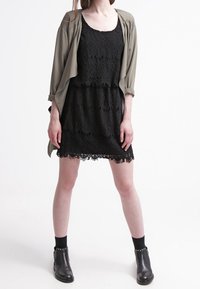 Svart spetsklänning med fransar längst ner, lager under en olivgrön öppen cardigan. Stylad med svarta ankelstövlar och strumpor.