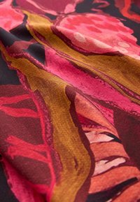 Gros plan sur un tissu avec un motif floral abstrait en nuances de rouge, rose, marron et orange, montrant la texture et les plis.