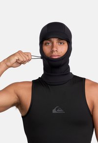 Black neoprene balaclava with adjustable drawstring, fitted design, and stitched accents, worn by a person in a black sleeveless top.