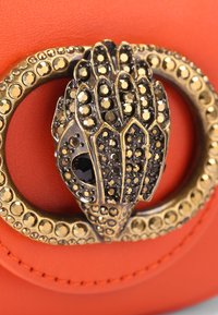 Borsa in pelle arancione con una chiusura in tonalità oro a forma di mano dettagliata, decorata con embellishments neri e dorati.