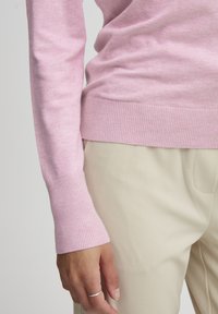 Suéter de punto acanalado en rosa claro con mangas largas, que presenta un puño ceñido. Combinado con pantalones taperos lisos en beige.