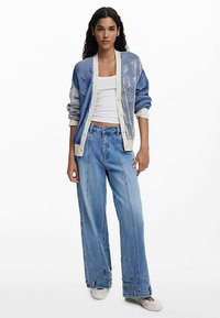 Sinine mustriline kardigan kreemika aktsentidega, kantud valge topi peal, kombineeritud lahtiste helesiniste teksade ja beežide kingadega.