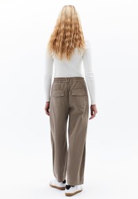 Lichtgrijs langemouwen top in combinatie met loszittende, beige cargobroek met twee achterzakken, elastische tailleband en witte sneakers.