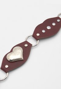 Burgundy bőr szíj ezüst szív díszítéssel, kerek fém gyűrűkkel és dekoratív szegecsekkel. Texturált felület sima fémes bevonattal.