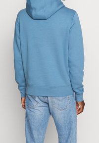 Blauwe fleece hoodie met een voorzak, een capuchon met trekkoord en geribbelde manchetten. Gecombineerd met lichtblauwe spijkerbroek.