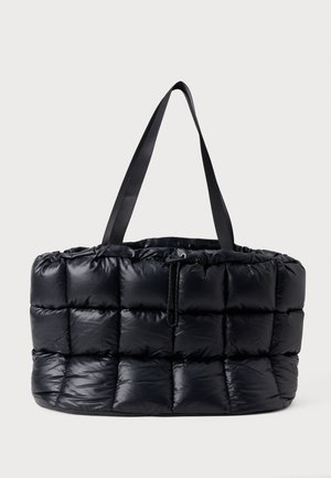 Sac cabas matelassé noir avec surpiqûres carrées gonflées, larges anses noires et fermeture à cordon en haut.