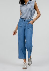 Vaqueros de pierna ancha azul claro con trabillas para cinturón, dos bolsillos delanteros y textura suave, combinados con un polo sin mangas a rayas en azul y blanco.