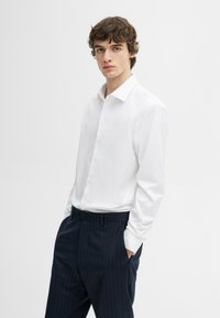 Witte longsleeve shirt met een puntkraag en knopen, gecombineerd met marineblauwe gestreepte broeken met een relaxte pasvorm.