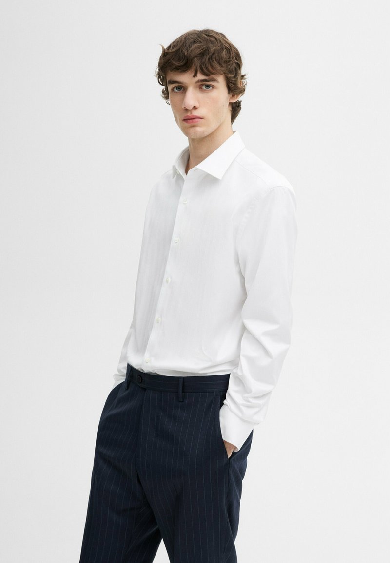 Witte longsleeve shirt met een puntkraag en knopen, gecombineerd met marineblauwe gestreepte broeken met een relaxte pasvorm.