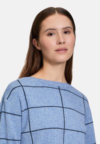 Blauer Pullover aus weichem Strickstoff mit einem Karomuster in Schwarz. Das Design verfügt über einen Bootsausschnitt und überschnittene Schultern.