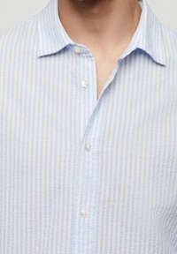 Světle modrá pruhovaná košile na knoflíky vyrobená z lehké látky, s špičatým límcem a texturovaným povrchem; obsahuje přední knoflíky a uvolněný střih.