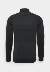 Chaqueta deportiva negra con cuello alto, mangas largas y tejido texturizado. Presenta un diseño de bloques de color con paneles en la parte posterior.