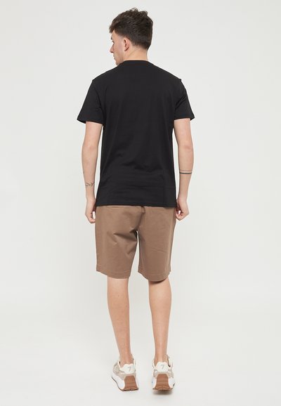 T-shirt en coton noir associé à un short marron. Le short a une coupe décontractée et arrive juste au-dessus du genou. Porté avec des baskets de couleur claire.