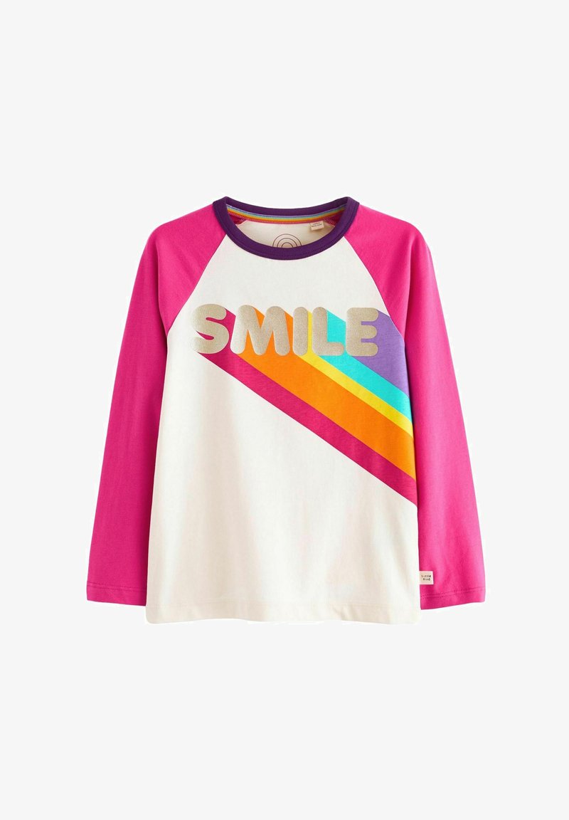 Hosszú ujjú fehér póló rózsaszín raglán ujjakkal. Az elülső részen a "SMILE" szó arany színben, valamint élénk narancs, kék és lila átlós csíkok díszítik.