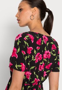 Vestido preto com flores vibrantes em tons de rosa e folhas verdes, com mangas curtas e um corte descontraído. Apresenta um decote redondo e cintura franzida.