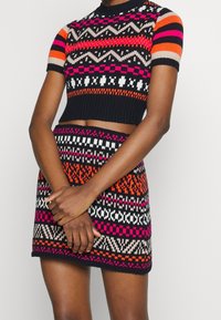 Neuleesta valmistettu crop-toppaja minihame-setti, jossa on monivärisiä geometrisia kuvioita mustana, oranssina, vaaleanpunaisena ja valkoisena; resoripintainen ja vartalonmyötäinen malli.